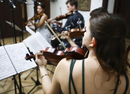 Fotografia. Koncert we wnętrzu Willi Decjusza. Muzycy grają na skrzypcach i wiolonczeli w Sali Balowej.